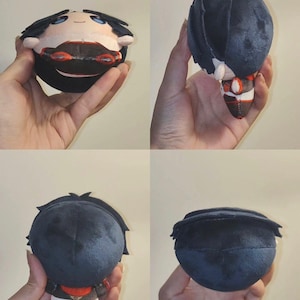 Pu&ograve; includere: Una bambola di peluche con un corpo rotondo e un design di personaggio. La bambola ha capelli neri, carnagione chiara e indossa un abito rosso e bianco. La bambola &egrave; tenuta in mano, mostrando i suoi dettagli da pi&ugrave; angolazioni.