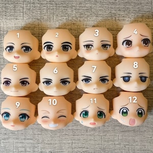Könnte beinhalten: Zwölf verschiedene leere Puppenköpfe mit bemalten Gesichtsausdrücken. Die Köpfe sind aus hellbeigem Kunststoff und haben verschiedene Augenfarben, Haarfarben und Gesichtsausdrücke. Die Köpfe sind von 1 bis 12 nummeriert.