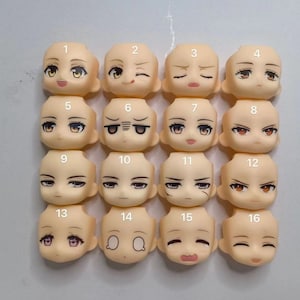 Op de afbeelding: Een set van 16 poppen gezichtsplaten met verschillende uitdrukkingen, genummerd van 1 tot en met 16. De gezichtsplaten zijn gemaakt van licht beige plastic en hebben geschilderde kenmerken.