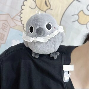 May include: A gray plush bird with a white ruffle around its neck. The bird has large black eyes and a small black beak.