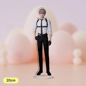 May include: An acrylic stand-up figure of a person wearing a white shirt, black trousers, and a black harness. The figure is 20 cm tall.