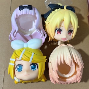 May include: Four anime-style character heads. One head is pink with a black bow, another is yellow with a black bow, and a third is yellow with a white bow. The fourth head is peach-colored.