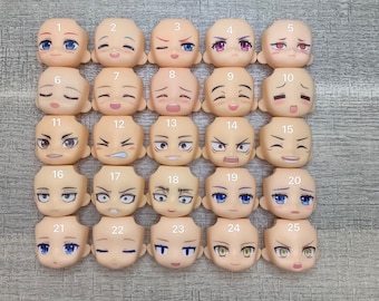 May include: Twenty-five different plastic doll heads with painted facial expressions. The heads are numbered 1 through 25.