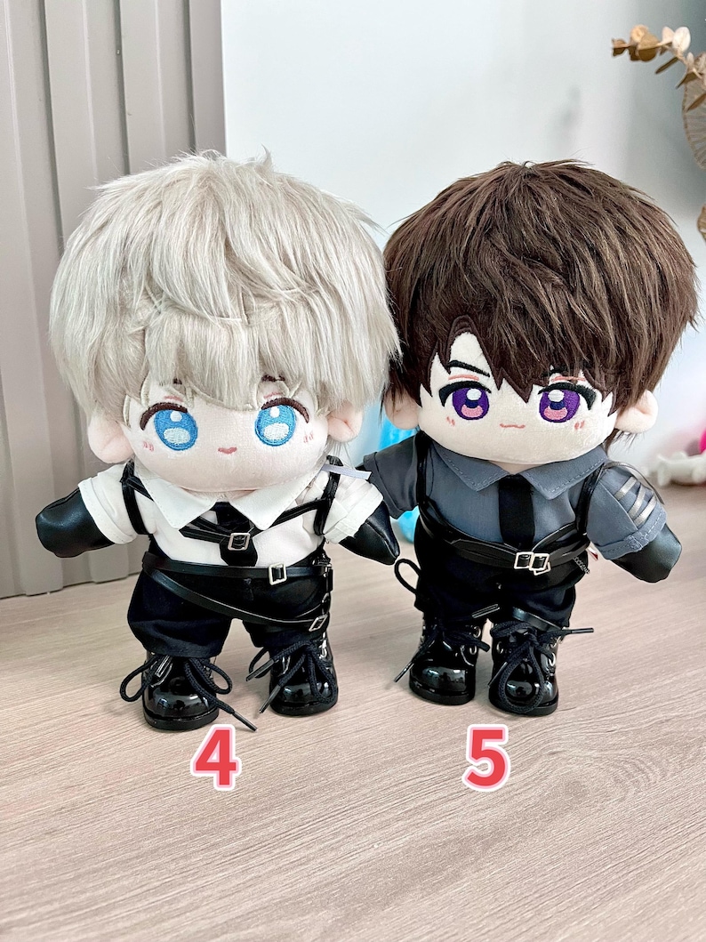 K&ouml;nnte beinhalten: Zwei Pl&uuml;schpuppen mit gro&szlig;en K&ouml;pfen und Augen im Anime-Stil. Eine Puppe hat silbernes Haar und tr&auml;gt ein wei&szlig;es Hemd, eine schwarze Hose und Stiefel. Die andere Puppe hat braunes Haar und tr&auml;gt ein graues Hemd, eine schwarze Hose und Stiefel. Beide Puppen haben schwarze G&uuml;rtel und die Zahlen 4 und 5 sind sichtbar.