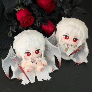 May include: Two plush dolls with white hair and red eyes, dressed in white outfits with attached wings. The dolls have a pale skin tone and are holding small, red-tipped swords. The background features red roses and dark foliage.