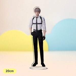 May include: An acrylic figure of a person wearing a white shirt, black trousers, and a black harness. The figure is standing on a clear acrylic base. The figure is 20 cm tall.