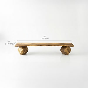 May include: A wooden bench with a natural live edge top and two geometric, faceted block legs. The bench measures 70 inches in length and 17 inches in width, featuring a warm brown wood grain pattern throughout the entire structure.