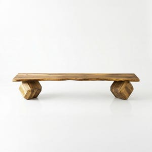 May include: A wooden bench with a natural edge top and geometric cube-shaped legs. The bench is made of light brown wood and has a minimalist design. The bench is approximately 60 inches long.