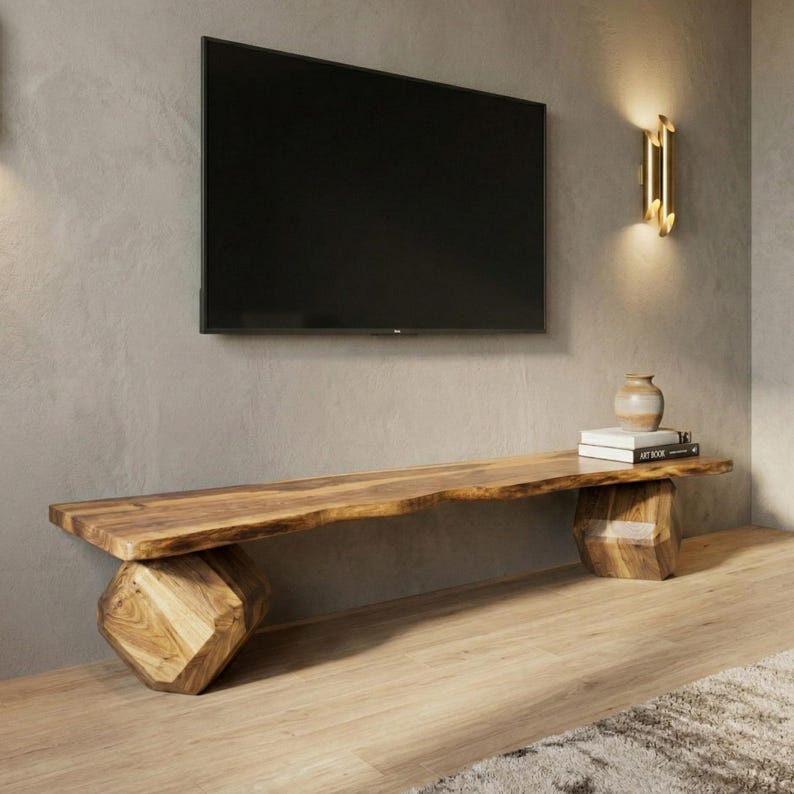 May include: A natural wood TV stand with a live edge top and geometric base. The stand is approximately 72 inches long. A flat-screen TV is mounted on the wall above the stand. A small vase and books are on the stand.