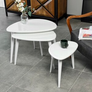 Puede incluir: Un conjunto de tres mesas nido blancas con una forma ovalada asim&eacute;trica &uacute;nica. Las mesas est&aacute;n hechas de material blanco brillante y tienen patas blancas delgadas.