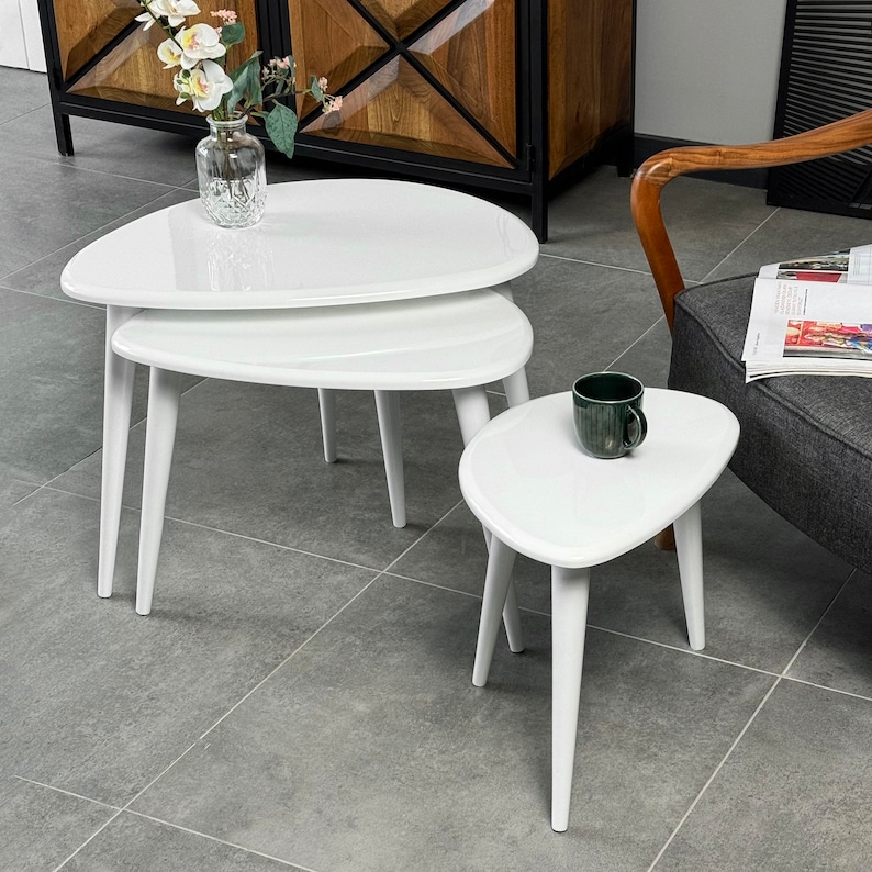 Puede incluir: Un conjunto de tres mesas nido blancas con una forma ovalada asim&eacute;trica &uacute;nica. Las mesas est&aacute;n hechas de material blanco brillante y tienen patas blancas delgadas.
