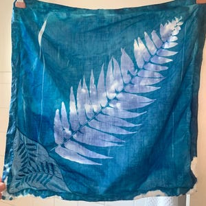 Könnte beinhalten: Ein quadratisches Stück Stoff in Tealblau mit einem weißen Farnblatt-Design darauf gedruckt. Der Stoff hängt an einer Wäscheleine.