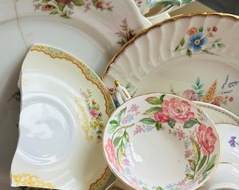 May include: A collection of vintage teacups and saucers with floral patterns. The teacups are white with gold trim and feature delicate floral designs in shades of pink, blue, and green. The saucers are also white with gold trim and feature similar floral designs.