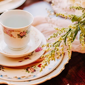 May include: A vintage teacup and saucer set with floral patterns in shades of pink, green, and gold. The set is placed on a stack of three plates with similar floral designs.