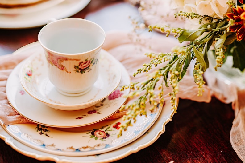 May include: A vintage teacup and saucer set with floral patterns in shades of pink, green, and gold. The set is placed on a stack of three plates with similar floral designs.