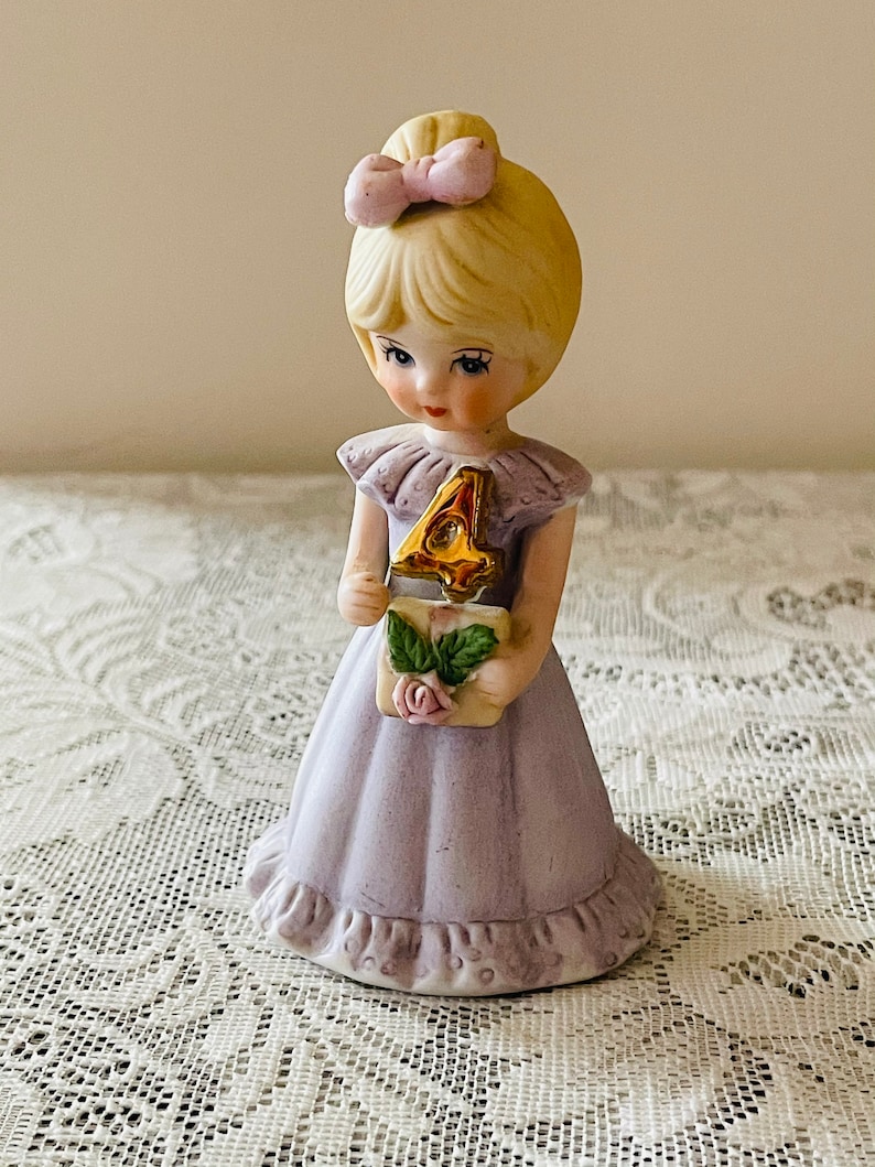 Vintage 4th Birthday Girl, A porcelain figurine of a little girl holding a small item with a rose design and a elegant gold number 4, wearing a light lavender dress.