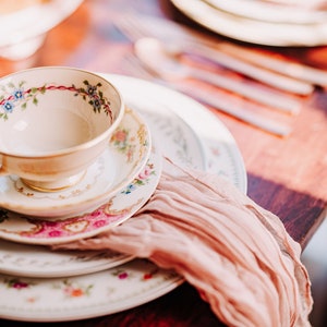 Vintage Mismatched teacup and Saucer and Dinner Plate stacked on each other set at a rustic wedding table with sheer fabric decor.
