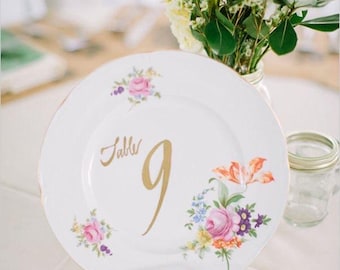 Platos de porcelana vintage desiguales para usar como números de mesa en una boda.
