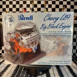 May include: A Revell model kit of a Chevy L89 Big Block Engine. The box features a detailed image of the engine, with chrome and orange components. Text on the box includes "No Painting" and "Easy Glue Assembly". The kit is for ages 10 and up.
