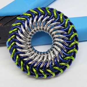 May include: A silver, blue, and green chainmail ring. The ring is made of small metal rings that are linked together in a pattern.