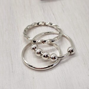 Puede incluir: Tres anillos de plata, uno con un dise&ntilde;o trenzado, otro con un dise&ntilde;o de cuentas y otro con una banda simple.