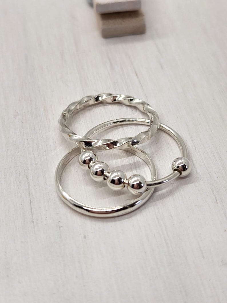 Puede incluir: Tres anillos de plata, uno con un dise&ntilde;o trenzado, otro con un dise&ntilde;o de cuentas y otro con una banda simple.