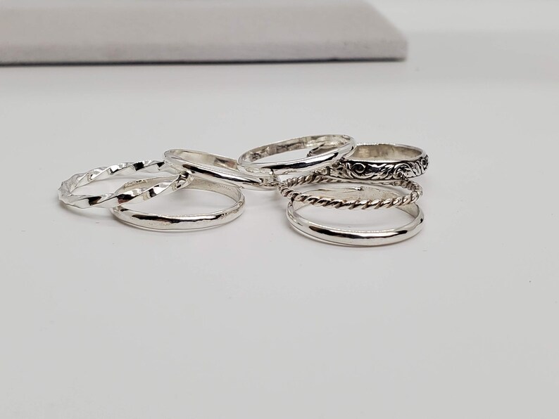 Puede incluir: Un conjunto de cinco anillos de plata, cada uno con un dise&ntilde;o diferente. Los anillos est&aacute;n apilados uno encima del otro, con el anillo m&aacute;s adornado en la parte superior.