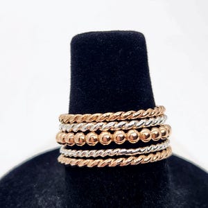 Puede incluir: Un conjunto de seis anillos apilables, con una mezcla de tonos plateados y oro rosa. Los anillos est&aacute;n hechos de alambre trenzado y dise&ntilde;os de cuentas.