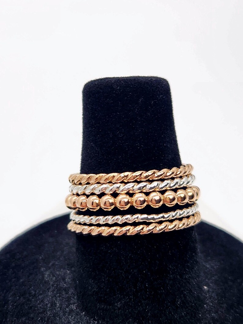 Puede incluir: Un conjunto de seis anillos apilables, con una mezcla de tonos plateados y oro rosa. Los anillos est&aacute;n hechos de alambre trenzado y dise&ntilde;os de cuentas.