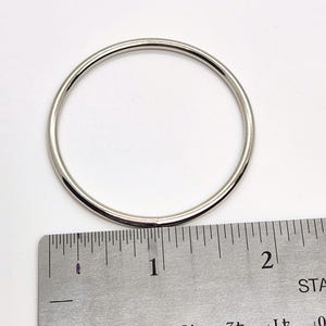 May include: A silver metal ring measuring 1 inch in diameter. The ring is shown next to a ruler for size reference.