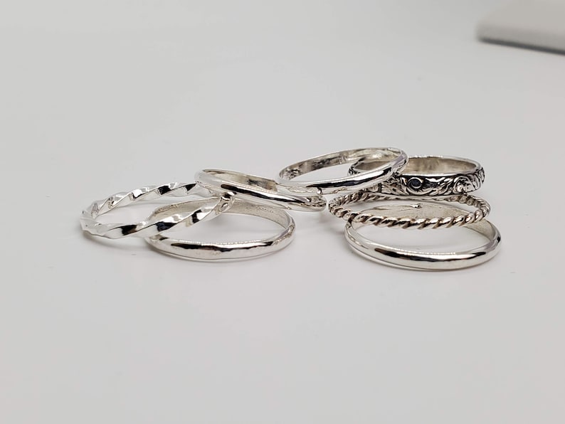 Puede incluir: Un conjunto de seis anillos de plata con diferentes texturas y dise&ntilde;os. Los anillos est&aacute;n apilados uno encima del otro.