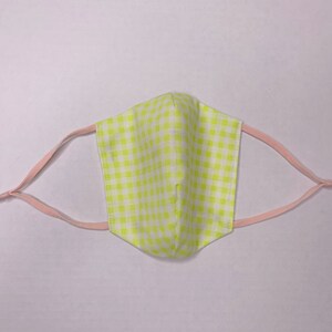 以下が含まれることがあります： ピンクのゴム製の耳ループが付いた黄色と白のギンガムチェックのフェイスマスクです。