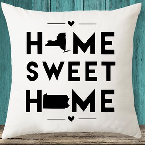 May include: White square pillow with the words "HOME SWEET HOME" in large black block letters. The word "HOME" features the silhouettes of New York and Pennsylvania. Small black hearts and lines are above and below the text.
