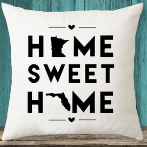 May include: White pillow with black text that reads "Home Sweet Home" with an outline of the state of Minnesota above the word "Home" and an outline of the state of Florida below the word "Home".