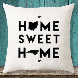 May include: White throw pillow with black text that reads "Home Sweet Home" with the state outlines of Ohio and North Carolina replacing the "O"s.