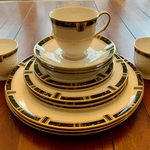 Könnte beinhalten: Ein Set aus weißem Porzellan-Geschirr mit einem schwarzen und goldenen Marmormuster. Das Set enthält eine Tasse, eine Untertasse und vier Teller.