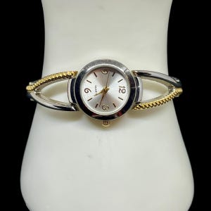 Può includere: Orologio al quarzo color argento e oro con quadrante rotondo. L'orologio ha un quadrante argentato con numeri neri alle 3, 6 e 12. Il cinturino è in stile bracciale argento e oro.
