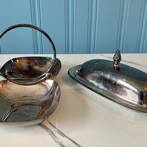 Könnte beinhalten: Zwei silberne Servierplatten, eine mit Griff und die andere eine Butterdose mit Deckel.
