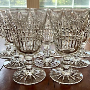 Może przedstawiać: Zestaw ośmiu przezroczystych szklanek do wina z ciętym wzorem. Szklanki mają wysoką, smukłą nóżkę i szeroką czaszę.