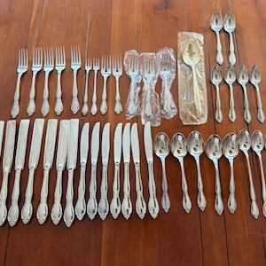 Peut inclure: Un ensemble de couverts argentés, comprenant des fourchettes, des couteaux et des cuillères, disposés sur une surface en bois. L'ensemble comprend des fourchettes et des cuillères de différentes tailles, ainsi que plusieurs couteaux. Certaines pièces sont emballées.