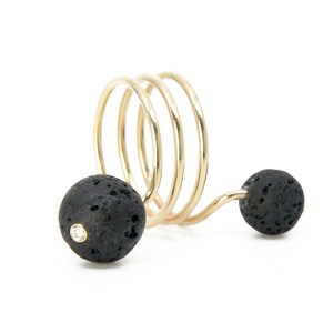 May include: A gold spiral ring with two black lava rock beads. One bead has a small diamond in the center.