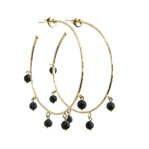 May include: Gold hoop earrings with black lava rock beads dangling from the bottom.