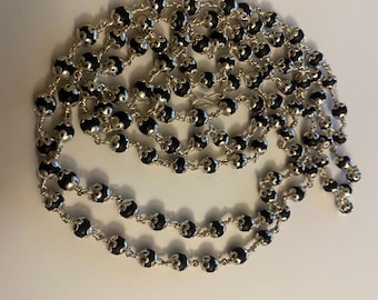 May include: A long silver chain necklace with black beads. Each bead has a silver design on it.