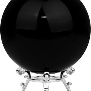 May include: A large, glossy black sphere, possibly a crystal ball, is displayed on an ornate silver-coloured metal stand. The sphere reflects light. The stand has a decorative, scrolled design.