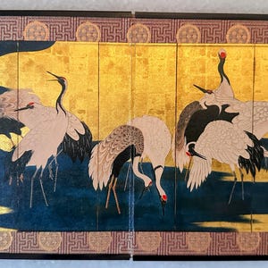 May include: A Japanese screen showing cranes. The artwork features cranes with red crowns, black and white feathers, and long necks. The background has a gold leaf design with a dark blue water scene.