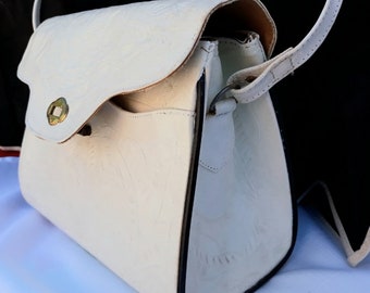 May include: A white leather handbag with a flap closure and a gold-toned clasp. The bag has a black trim and a white leather strap.