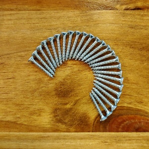 May include: A close-up of a group of silver screws arranged in a semi-circle on a wooden surface.