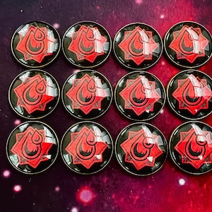 May include: Twelve circular buttons arranged in a grid, each featuring a glossy, domed surface. The design consists of a black background with a red, stylised flame or droplet icon centred within a geometric, star-like shape with sharp points.