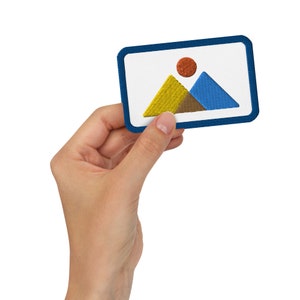 May include: A blue, yellow and orange embroidered patch with a mountain range design. The patch is being held in a hand.