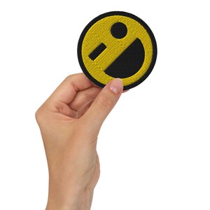 May include: A yellow smiley face embroidered on a black fabric patch.